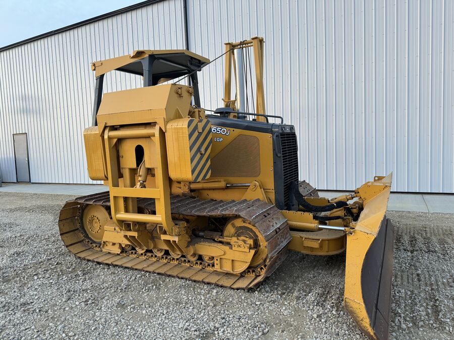 A low-ground-pressure dozer on gravel beside a shop wall, blade down, rear three-quarter