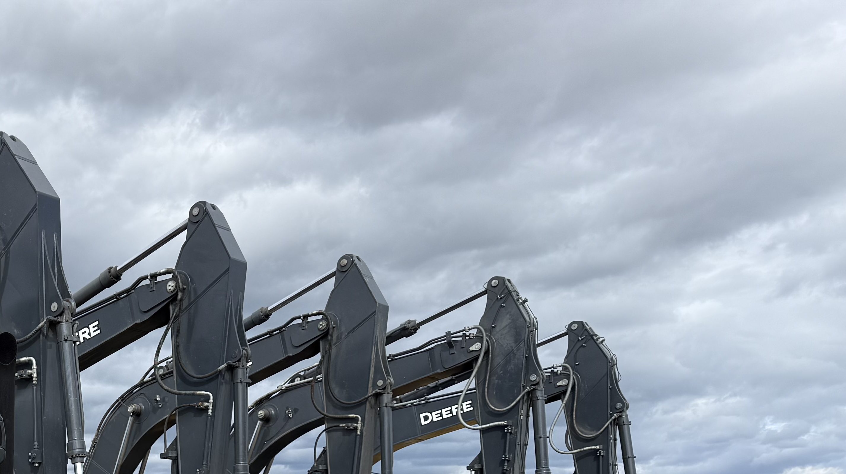 A row of excavators, booms raised against an overcast sky