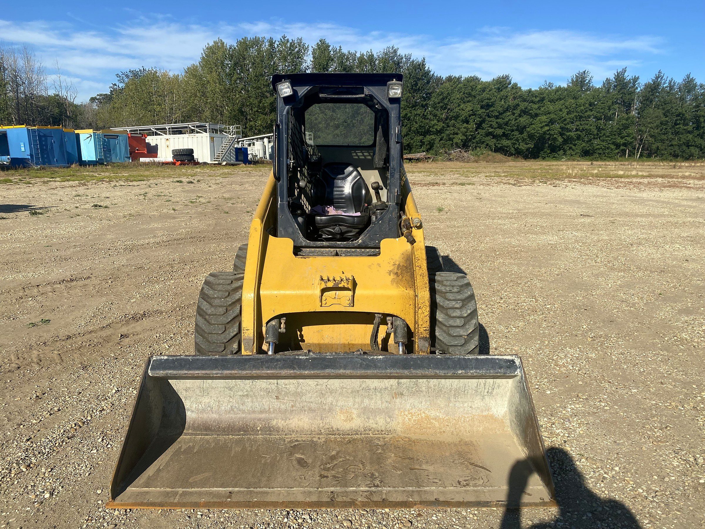 A skid steer head on in the yard, bucket flat on the gravel